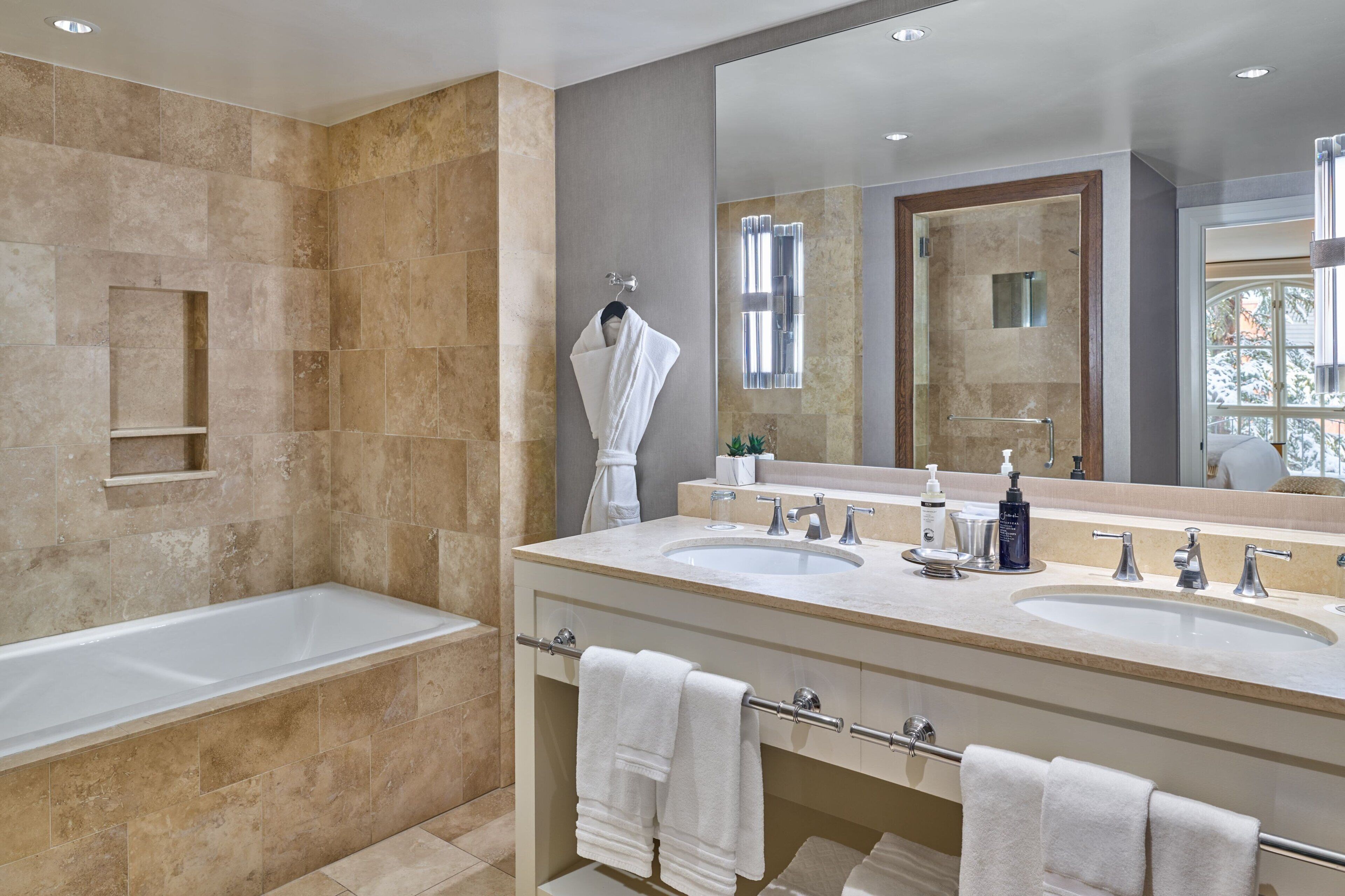 A modern bathroom with a large bathtub, two sinks, and a large mirror.