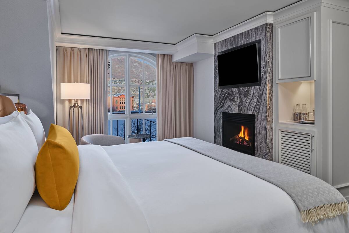 A hotel room with a large bed, a fireplace, a television, and a view of a cityscape.