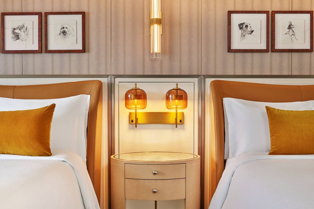 A hotel room with two beds, a bedside table with a lamp, and framed artwork on the wall.