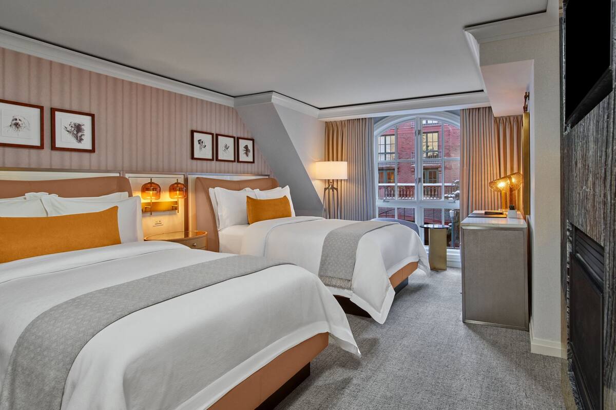 A hotel room with two beds, a desk, and a large window with a view of a building.