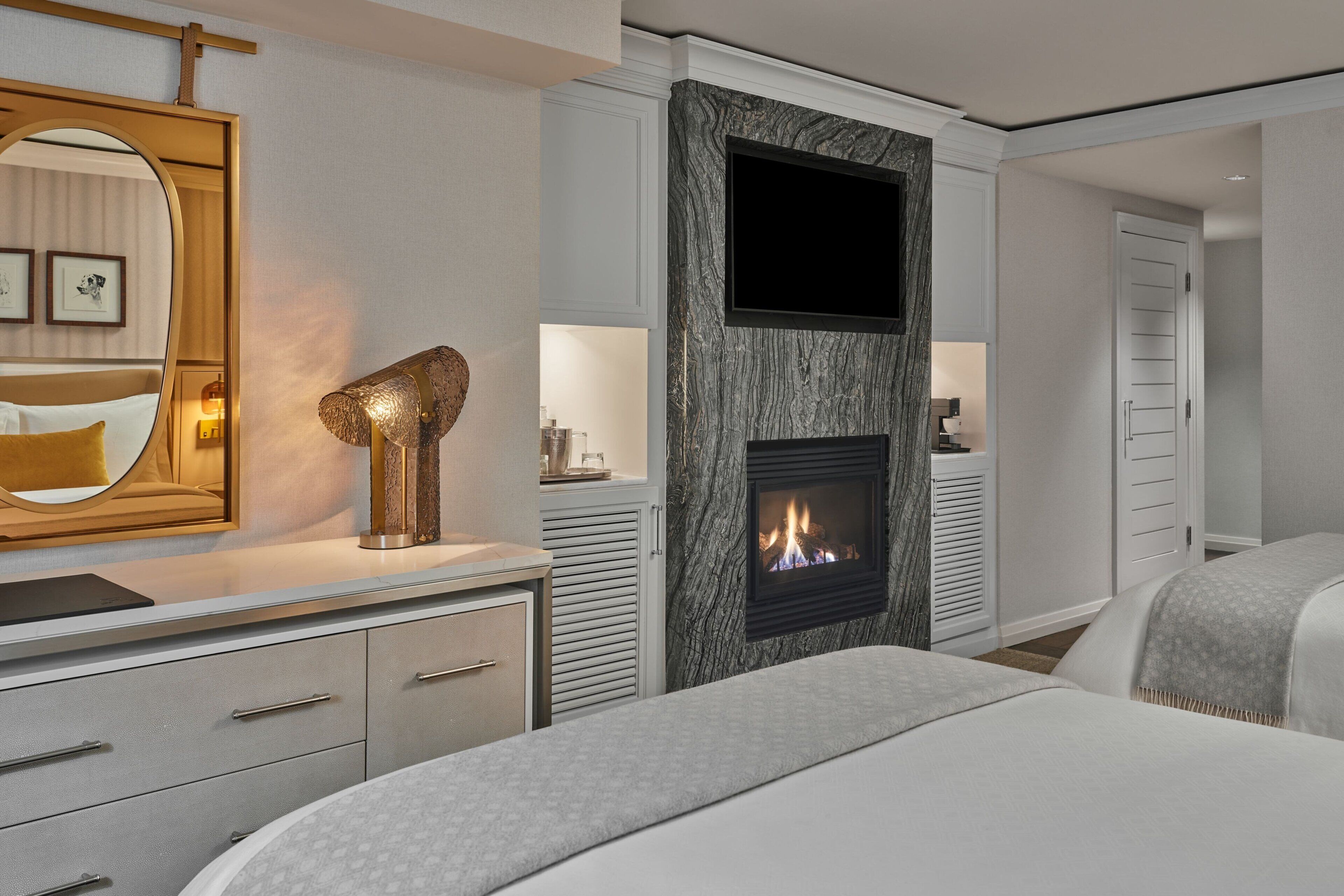 Quarto de hotel moderno com lareira, um espelho grande e uma cama com colcha estampada.