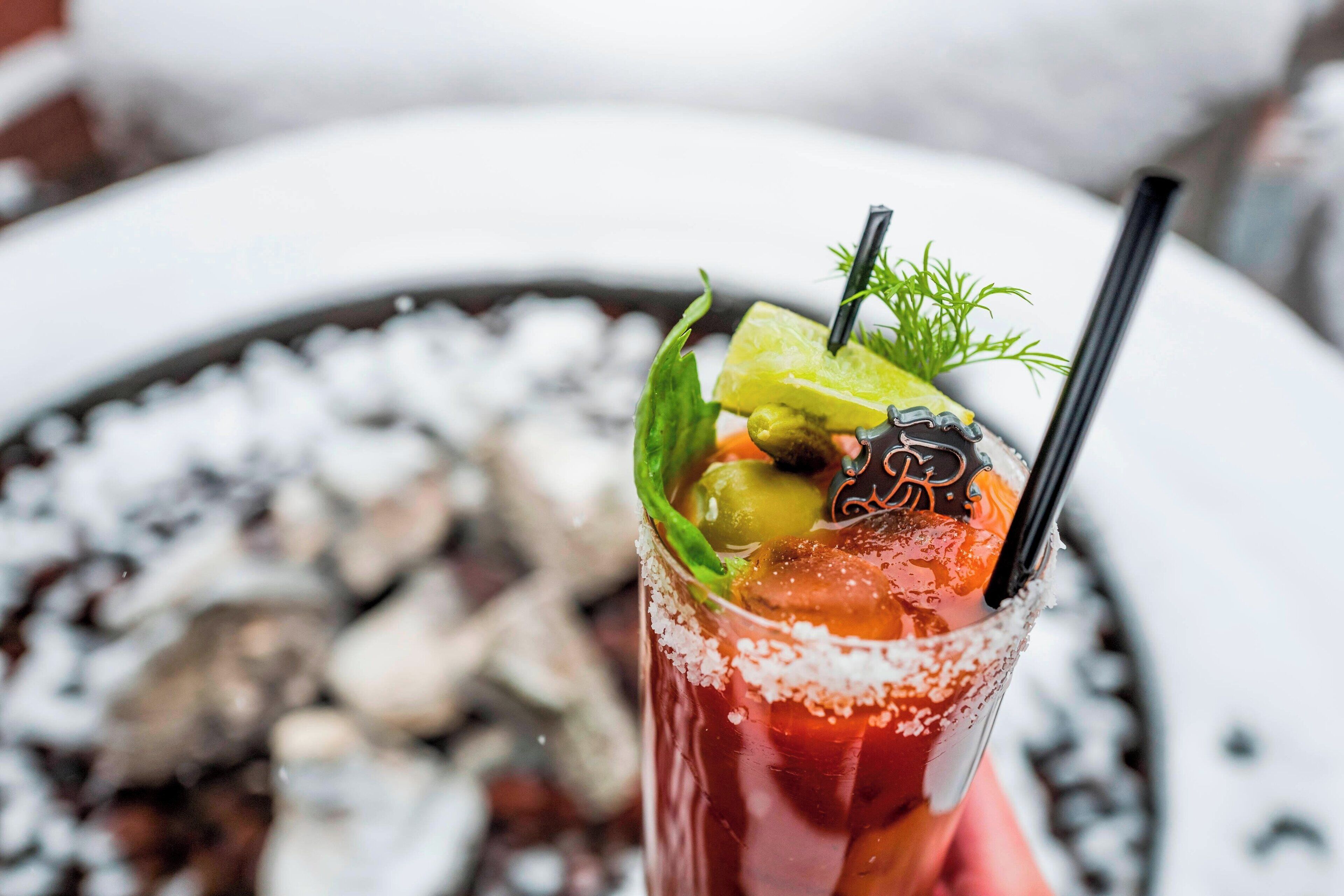 A Bloody Mary cocktail garnished with lime, olives, and a sprig of dill, served in a glass with a salted rim.
