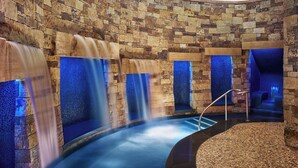 A spa area with stone walls, a curved water feature, and a seating area with a blue-lit backdrop. - The St. Regis Aspen Resort (Aspen)