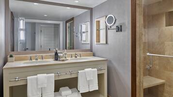 A modern bathroom with two sinks, a large mirror, a handheld mirror, and a glass-enclosed shower.
