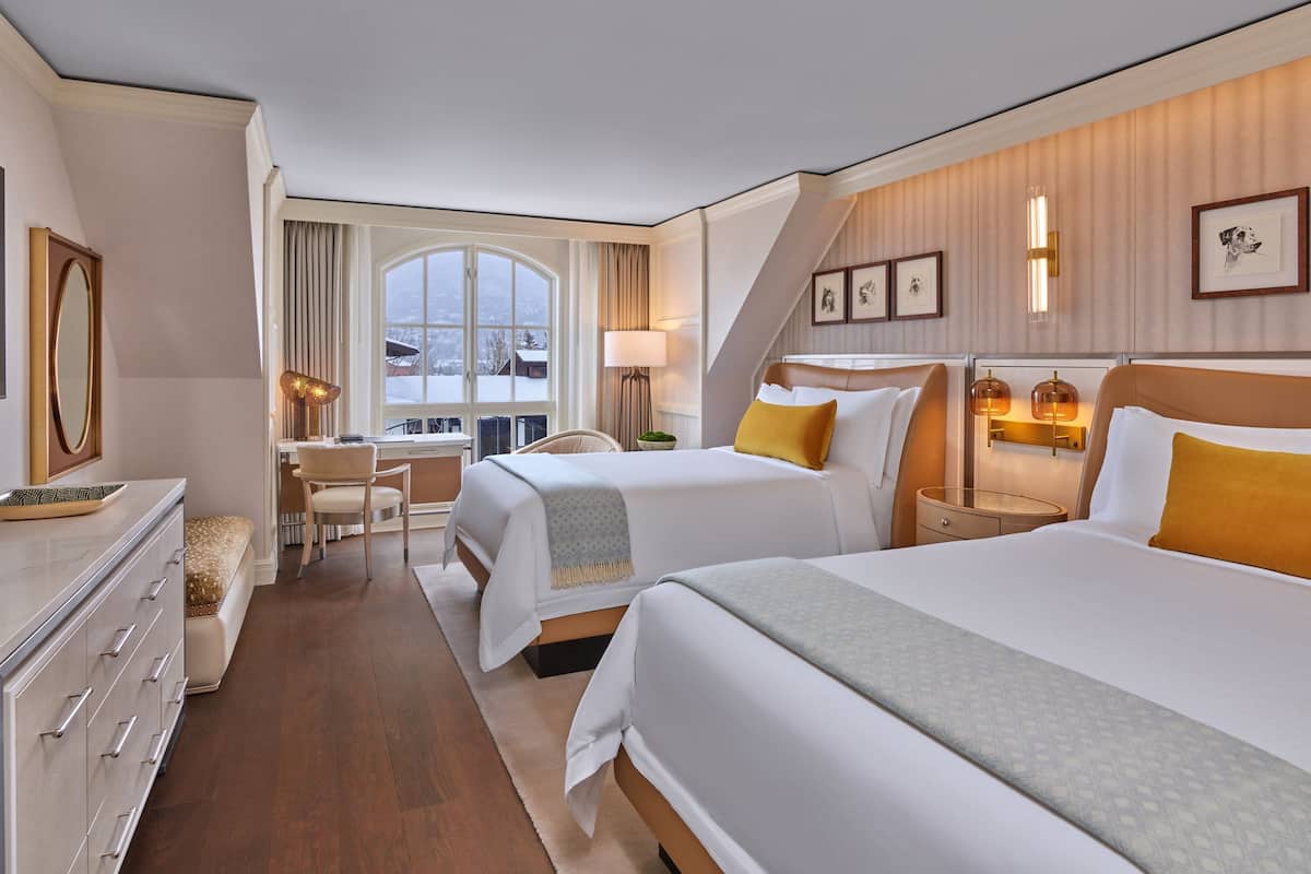 A hotel room with two beds, a desk, and a large window.