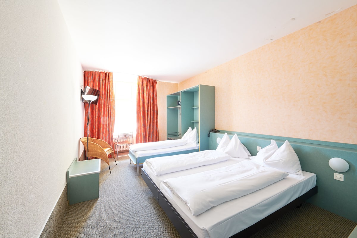 A hotel room with two single beds, a small desk, a chair, and a wardrobe.