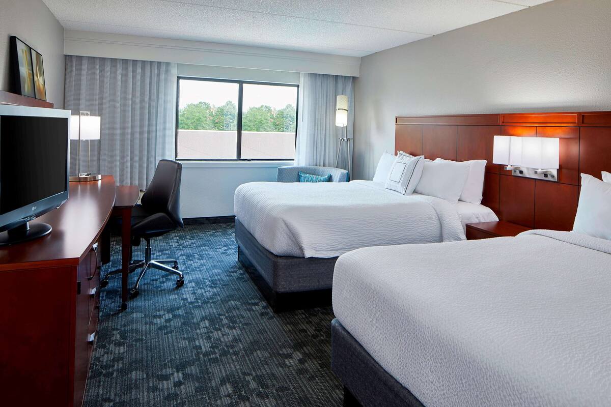 A hotel room with two beds, a desk with a TV, and a view of the outdoors.