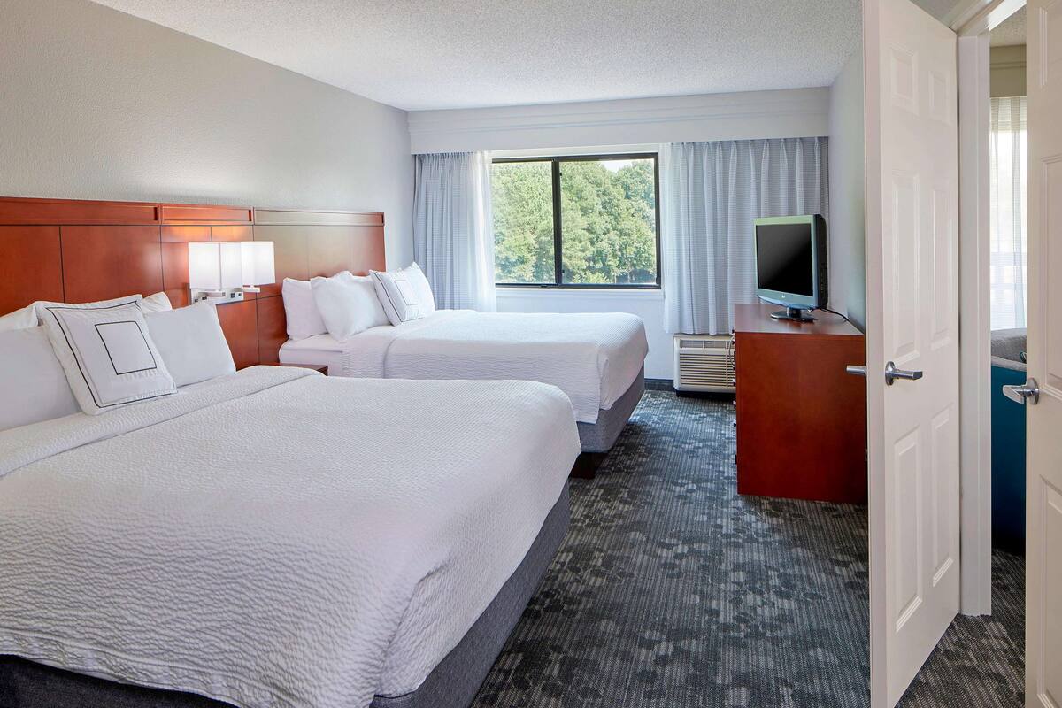 A hotel room with two beds, a television, and a window with curtains.