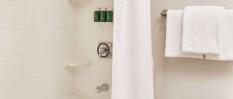 A bathroom with a bathtub, a shower curtain, a towel rack with towels, and toiletries on the wall.