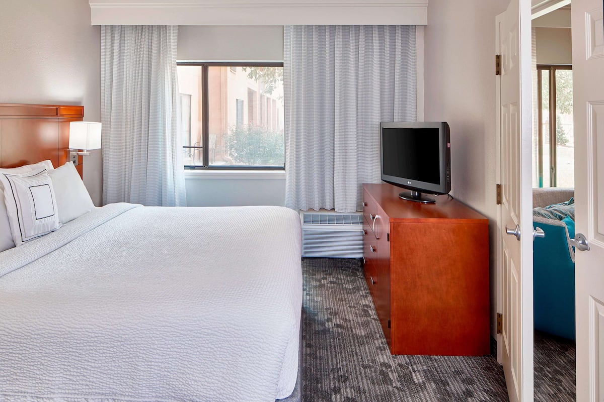A hotel room with a large bed, a TV on a wooden dresser, and a view of the outdoors through the window.