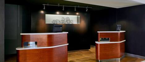 A reception area with two wooden reception desks, a modern light fixture, and a wall-mounted artwork.