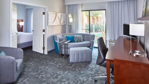 A hotel room with a gray sofa, a gray armchair, a small table, a desk with a lamp, and a large window with curtains. - Sonesta Select Raleigh Durham Airport Morrisville (Morrisville)