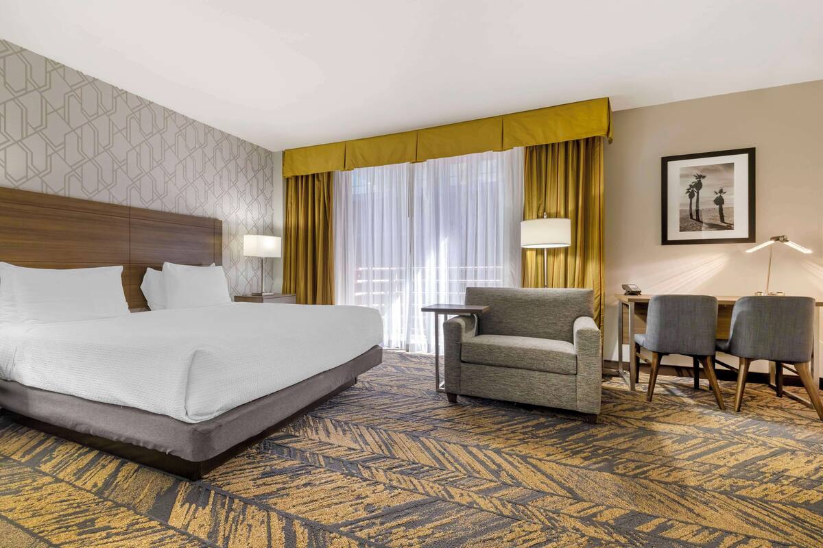 Une chambre d’hôtel avec un grand lit, un canapé, deux fauteuils, une petite table et un tableau encadré au mur.