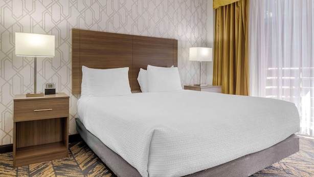 Una habitación de hotel con una cama grande, dos mesitas de noche, un cabecero y un papel tapiz estampado.