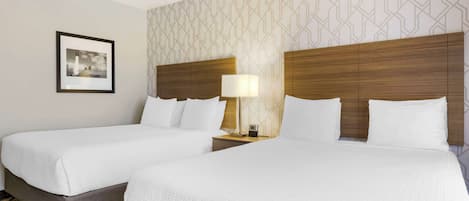 A hotel room with two beds, a framed picture on the wall, and a patterned wallpaper.