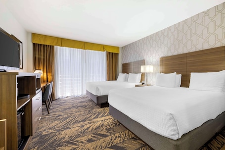 A hotel room with two beds, a desk, a television, and a patterned carpet.