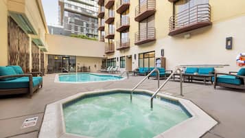 A rooftop pool area with lounge chairs, a hot tub, and a view of a high-rise building.