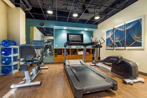 Une salle de sport équipée de tapis de course, de vélos d’exercice et d’un écran fixé au mur.