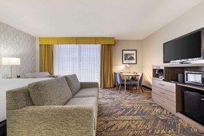 A hotel room with a sofa, a dining table with chairs, a TV, a refrigerator, and a patterned carpet. - Best Western Plus Bayside Inn (San Diego)
