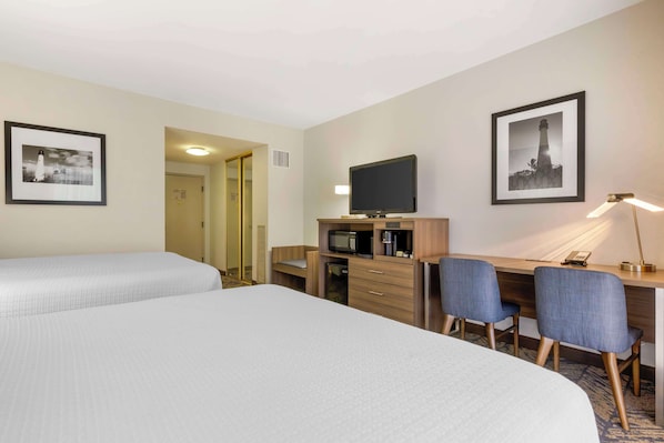Une chambre d’hôtel avec deux lits, un bureau avec un ordinateur, une télévision et une lampe.