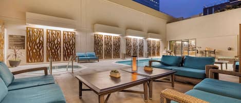 Zona junto a la piscina con mobiliario de mimbre, una piscina y un edificio al fondo.