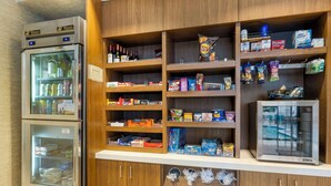 Una kitchenette con refrigerador, microondas y gabinetes de madera que contienen diversos alimentos y bebidas.