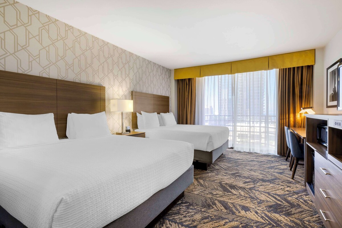 A hotel room with two beds, a desk with a chair, a TV, and a patterned carpet.