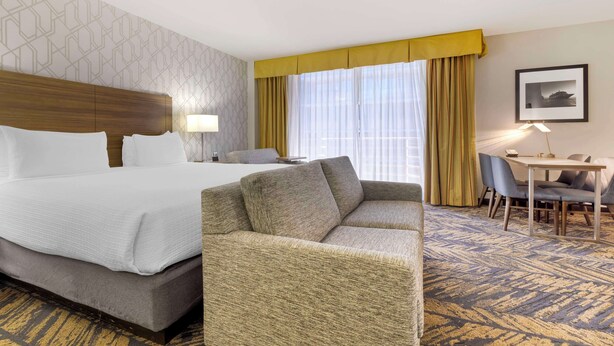 A hotel room with a bed, a sofa, a dining table with chairs, and a window with curtains. - Best Western Plus Bayside Inn (San Diego)