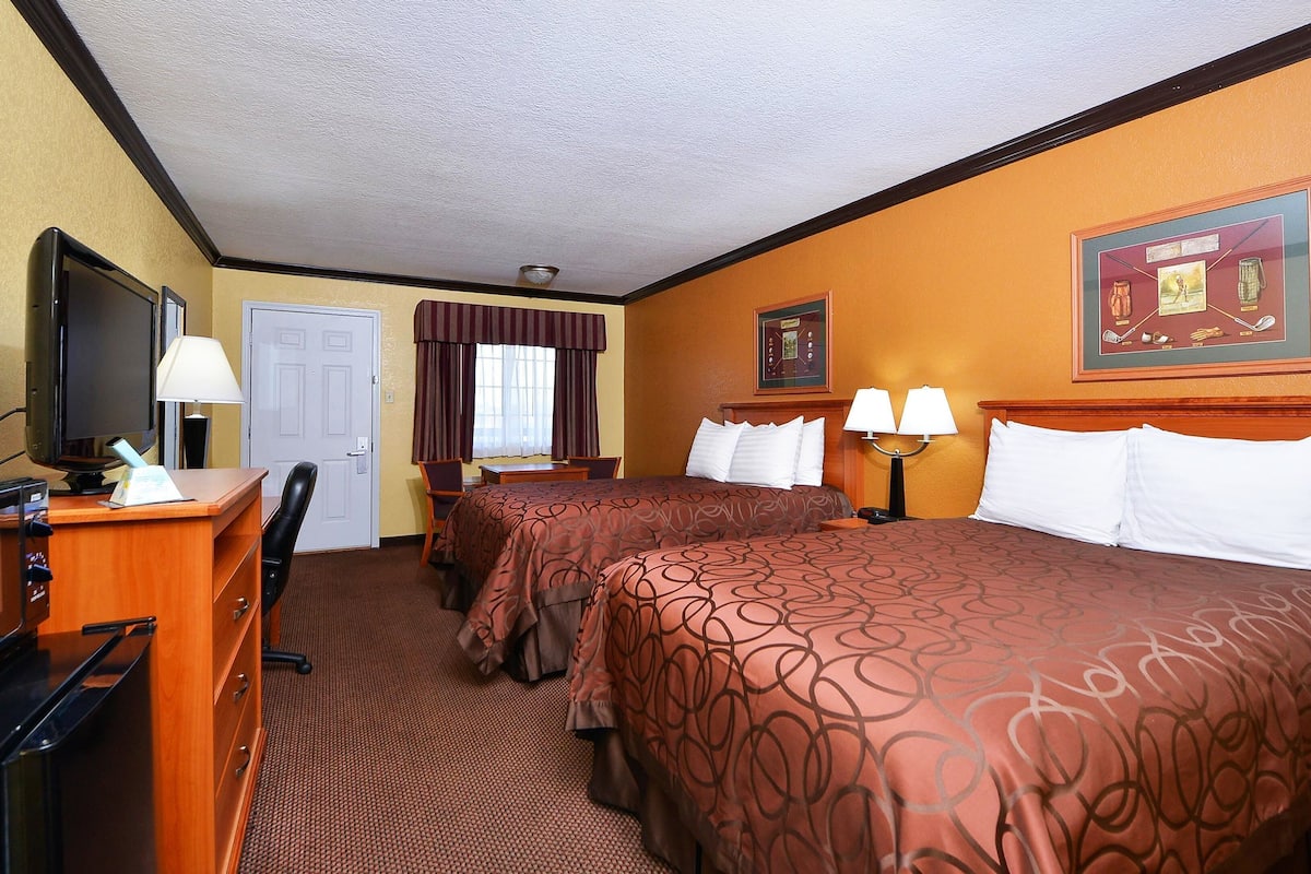 A hotel room with two beds, a desk with a computer, a TV, and a door.