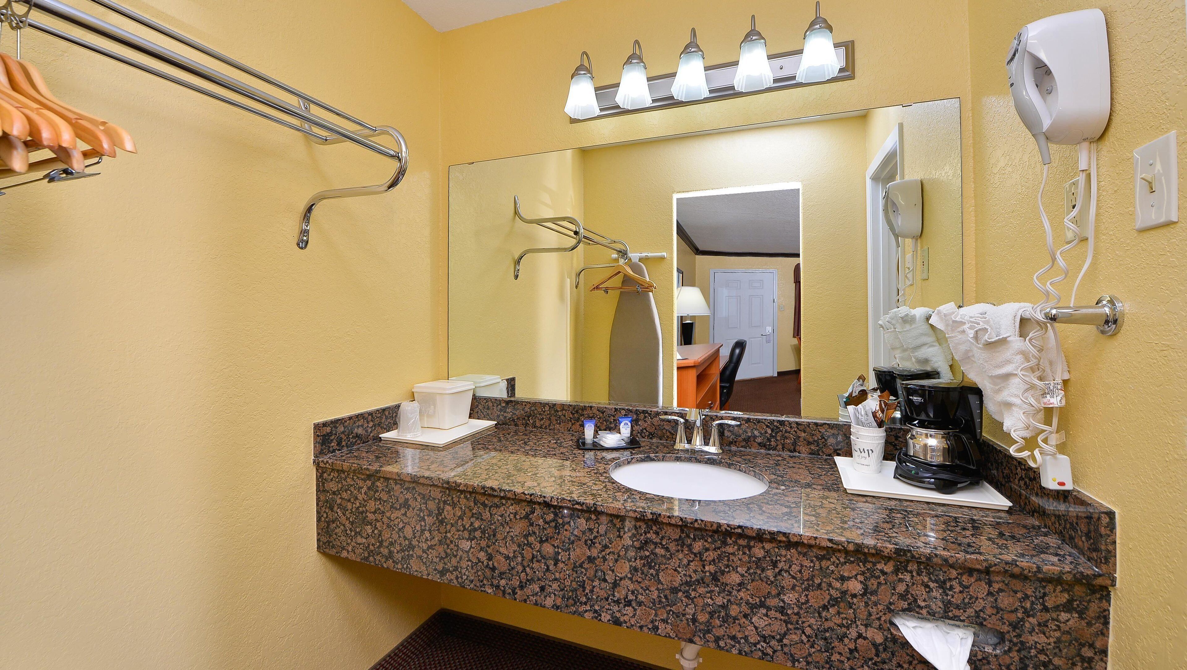 Un baño con encimera de granito, un lavamanos, un espejo, toallero, secador de pelo y cafetera.