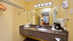 A bathroom with a granite countertop, a sink, a mirror, a towel rack, a hairdryer, and a coffee maker.