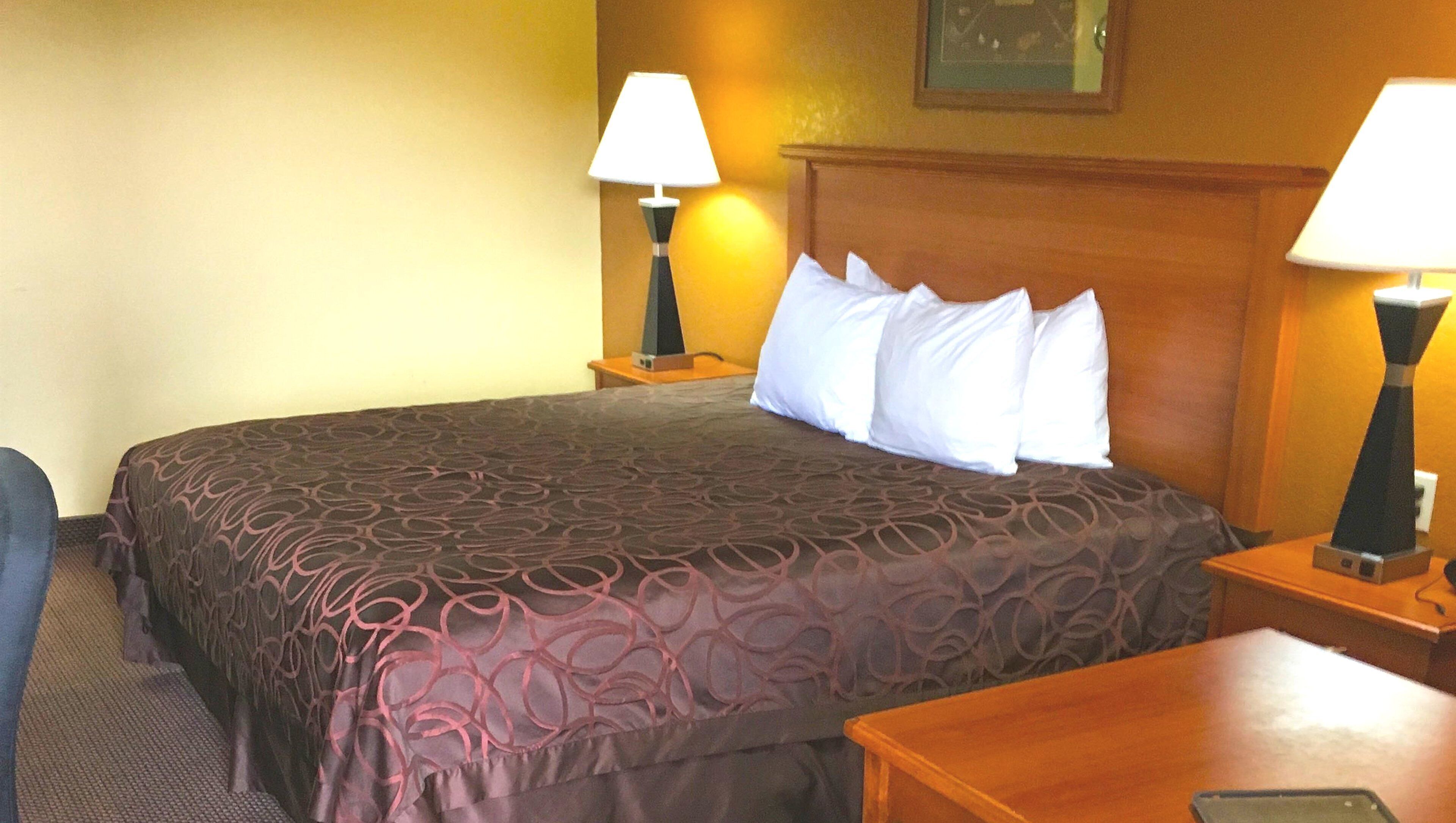 A hotel room with a large bed, two bedside lamps, a wooden headboard, and a small table with a lamp.