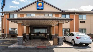 A Comfort Inn hotel with a covered entrance, a parking lot, and a white car parked in front.