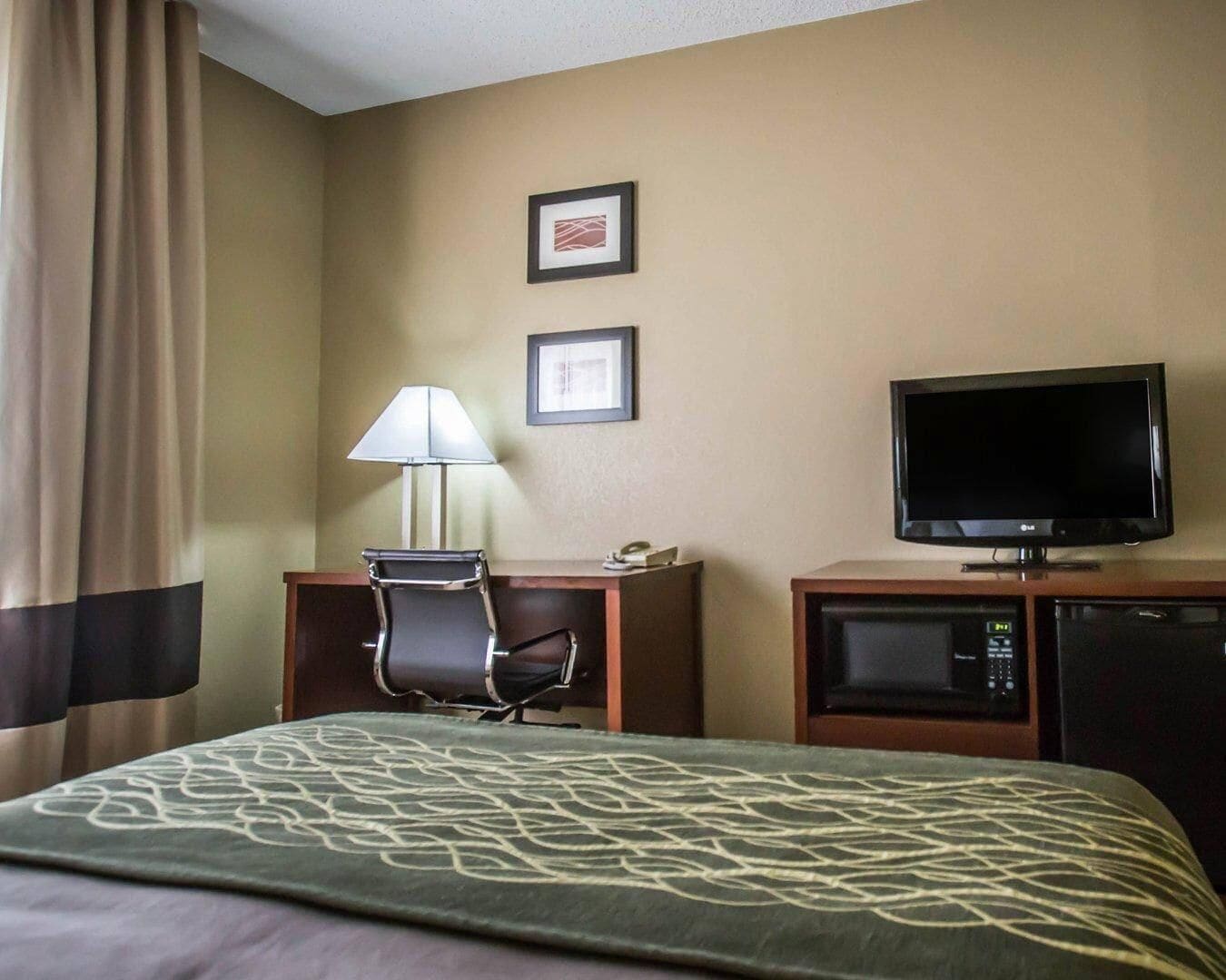 A hotel room with a bed, a desk with a lamp, a television, and a microwave.