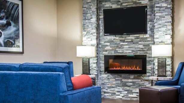 A living room with a stone fireplace, a flat-screen TV, blue sofas, and a patterned rug.