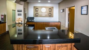 A hotel reception area with a black counter, wooden cabinets, a sign for Comfort INN, and a framed commitment sign.