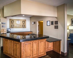 A hotel lobby with a reception desk, a wooden cabinet with a black countertop, and a wall-mounted sign that reads 'Comfort Inn.'