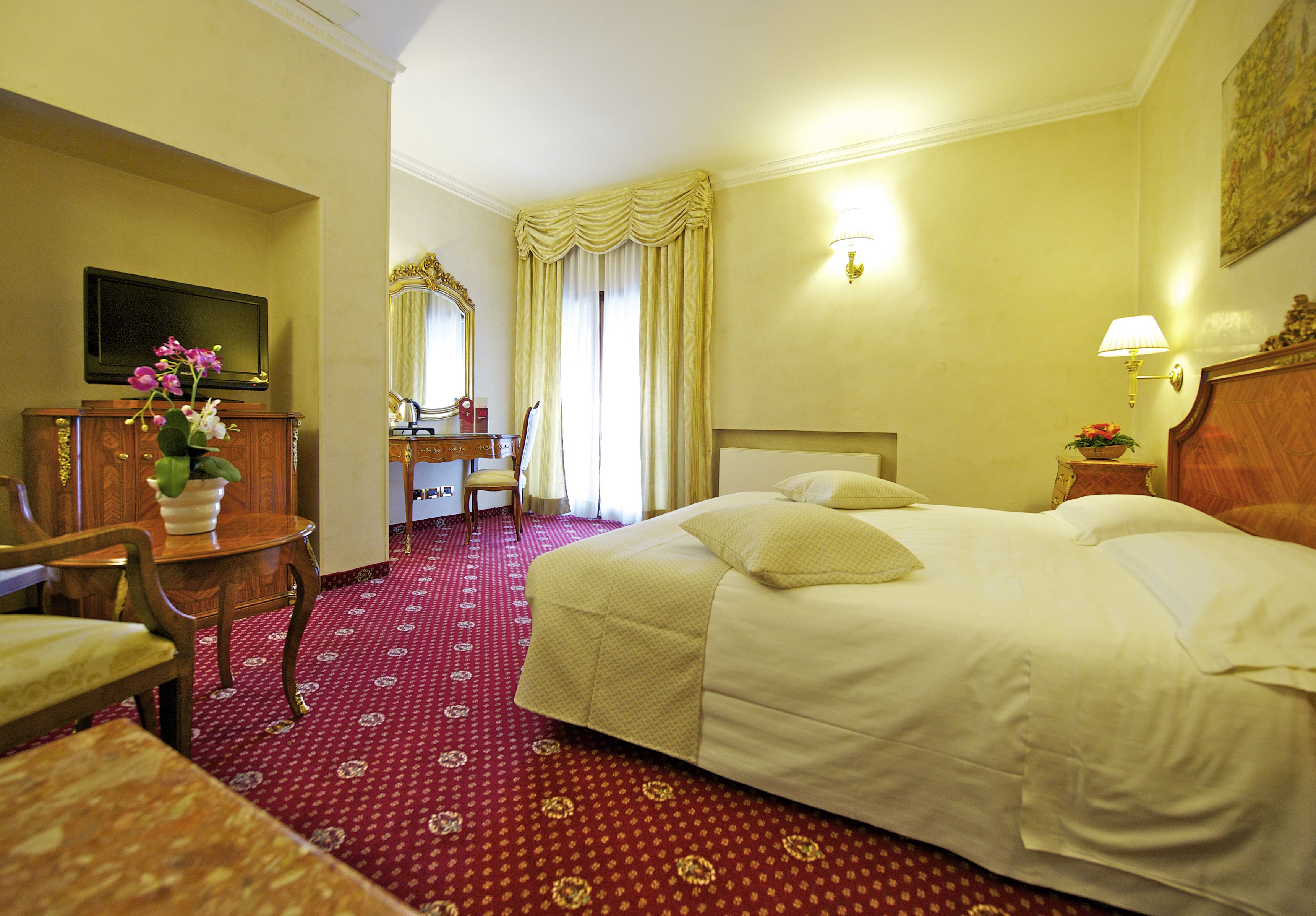 Una habitación de hotel con cama, escritorio, silla, televisión y espejo.