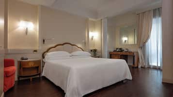 Ein Hotelzimmer mit einem großen Bett, Nachttischen, einem Schreibtisch, einem Sessel, einem Spiegel und einem Fenster mit Vorhängen.