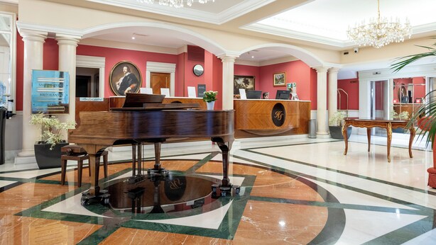 A grand lobby with a grand piano, a reception desk, and a chandelier.