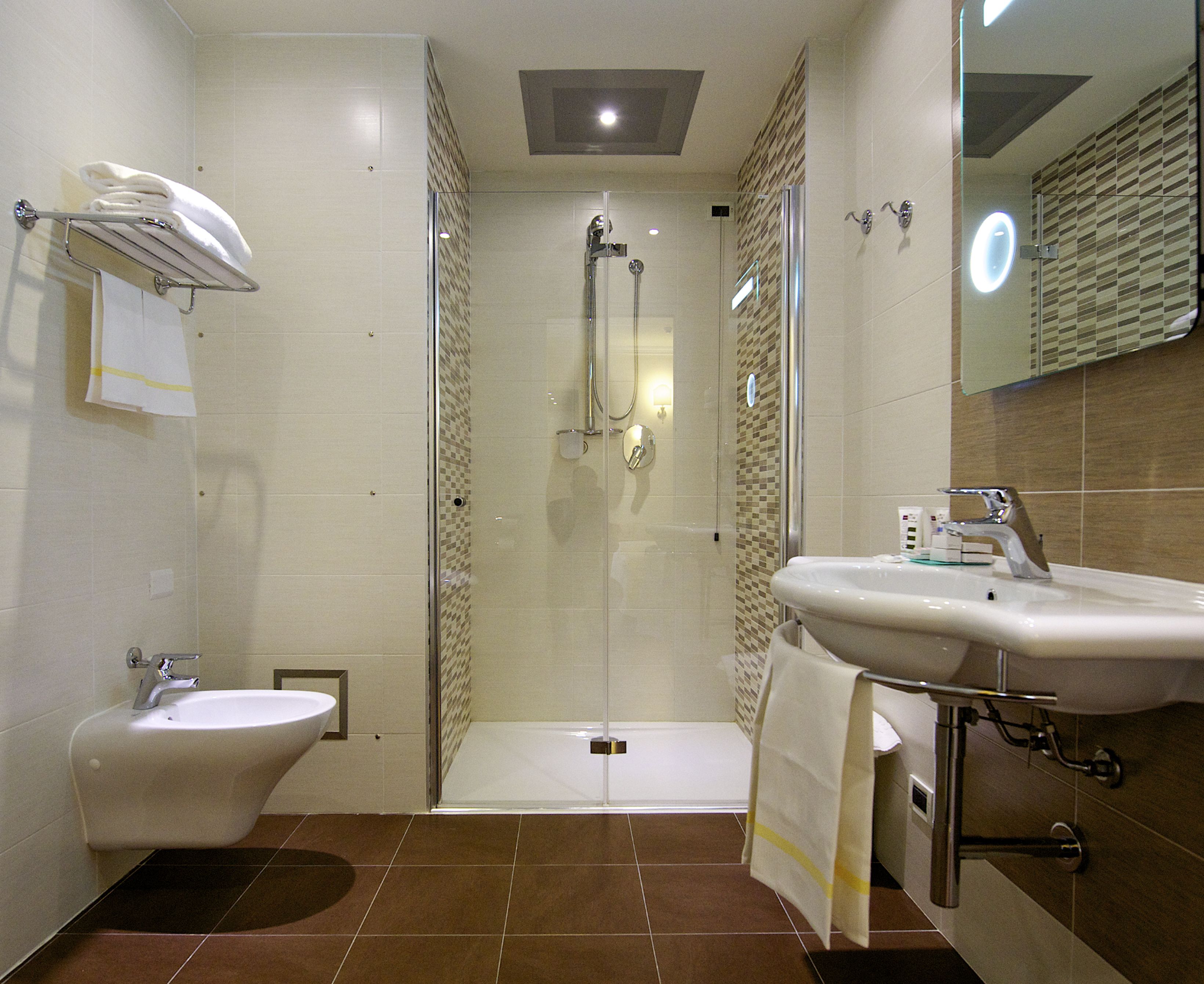 Un baño moderno con ducha envuelta en vidrio, lavamanos pedestal y bidé.
