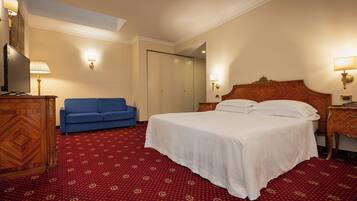 A hotel room with a large bed, a blue sofa, a wooden dresser, and a red patterned carpet.