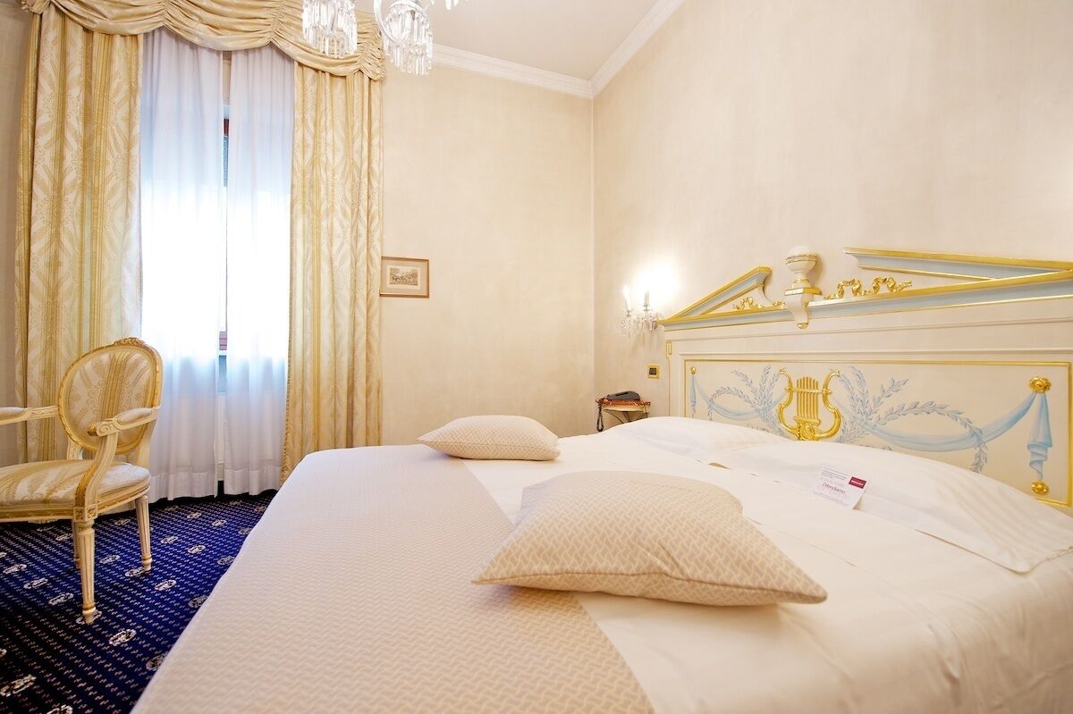 A hotel room with a large bed, a chair, a desk, and a chandelier.