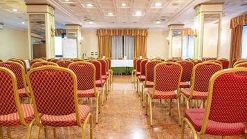 Un salón de conferencias con hileras de sillas rojas y doradas, una mesa blanca y un suelo de mármol.