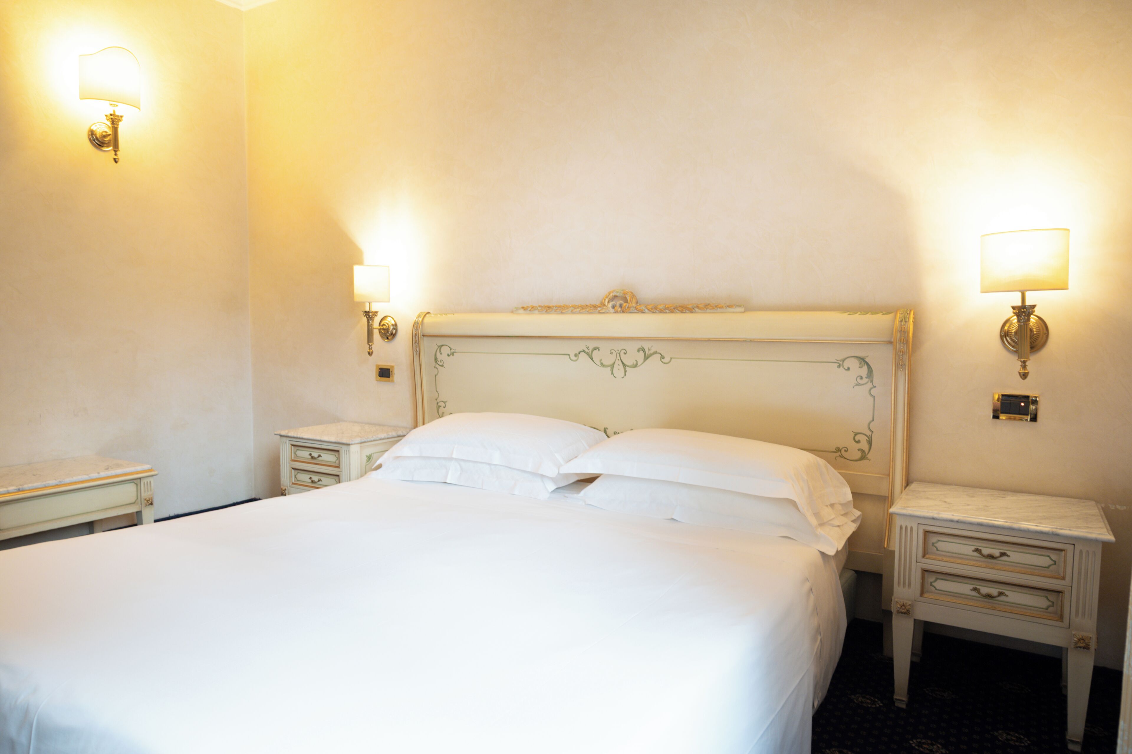 A neatly made bed with white linens and two bedside tables with lamps.