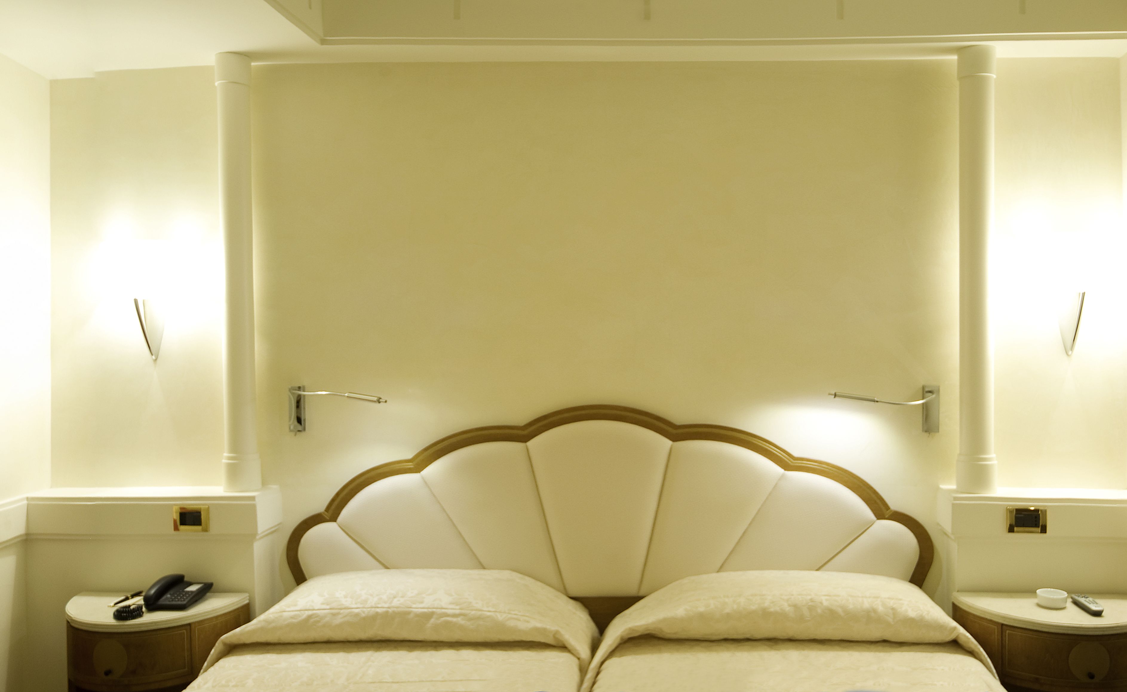 A hotel room with a large bed, bedside tables, and wall-mounted lamps.