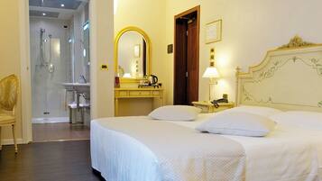 Habitación de hotel con una cama grande, una mesita de noche con lámpara, un espejo y un baño visible a través de una puerta abierta.