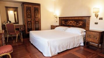 A large bed with a wooden headboard, a wooden wardrobe, a desk with a chair, and two wall-mounted lamps.