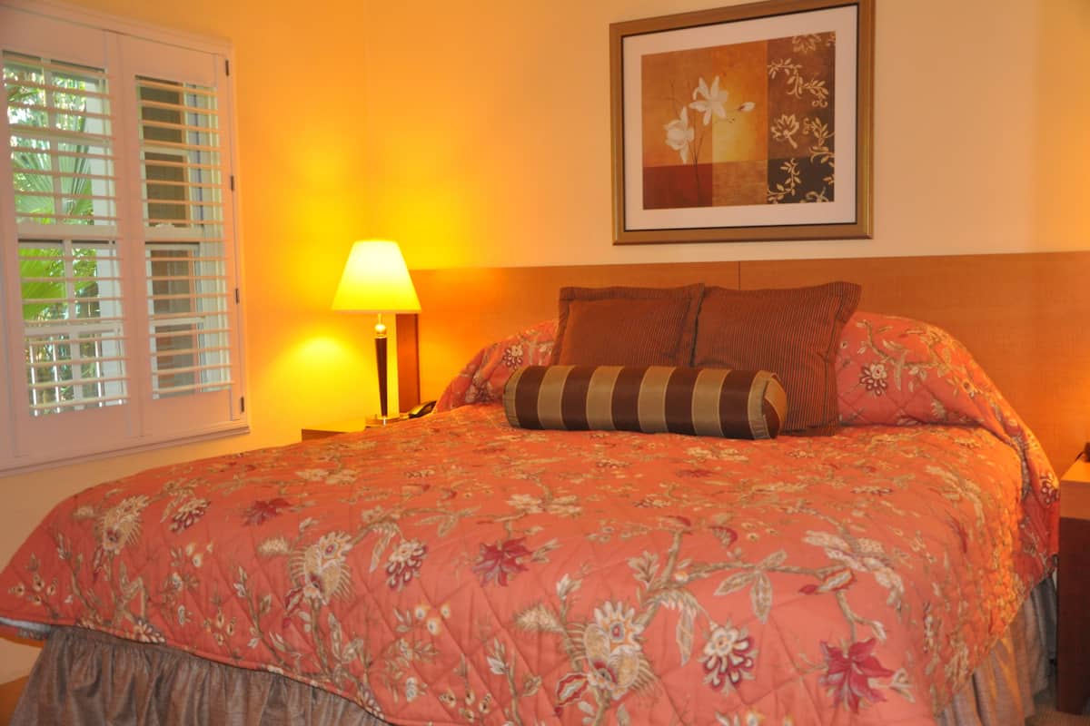 A bedroom with a floral bedspread, a bedside lamp, and a framed picture on the wall.
