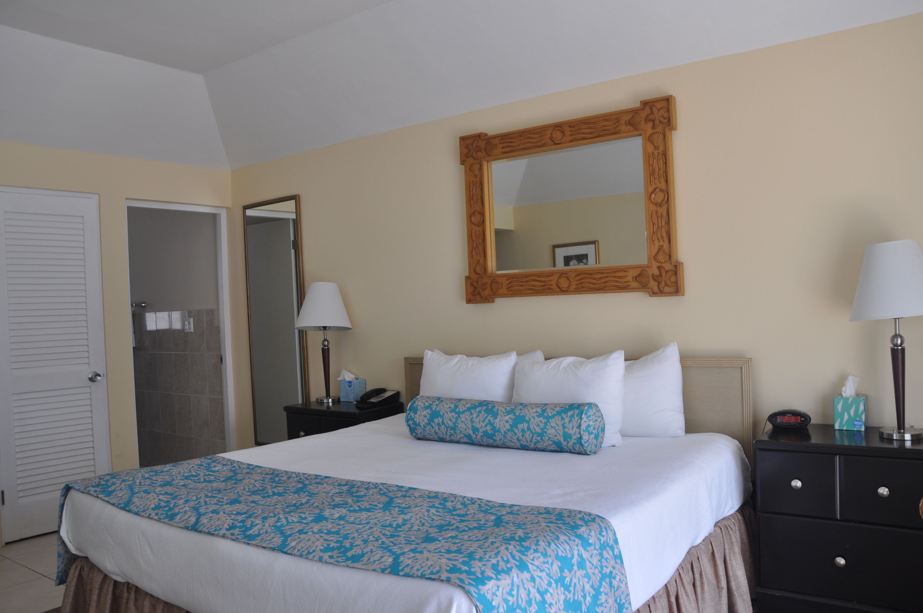 Una habitación de hotel con una cama, una mesita de noche, un aparador, un espejo y una puerta.